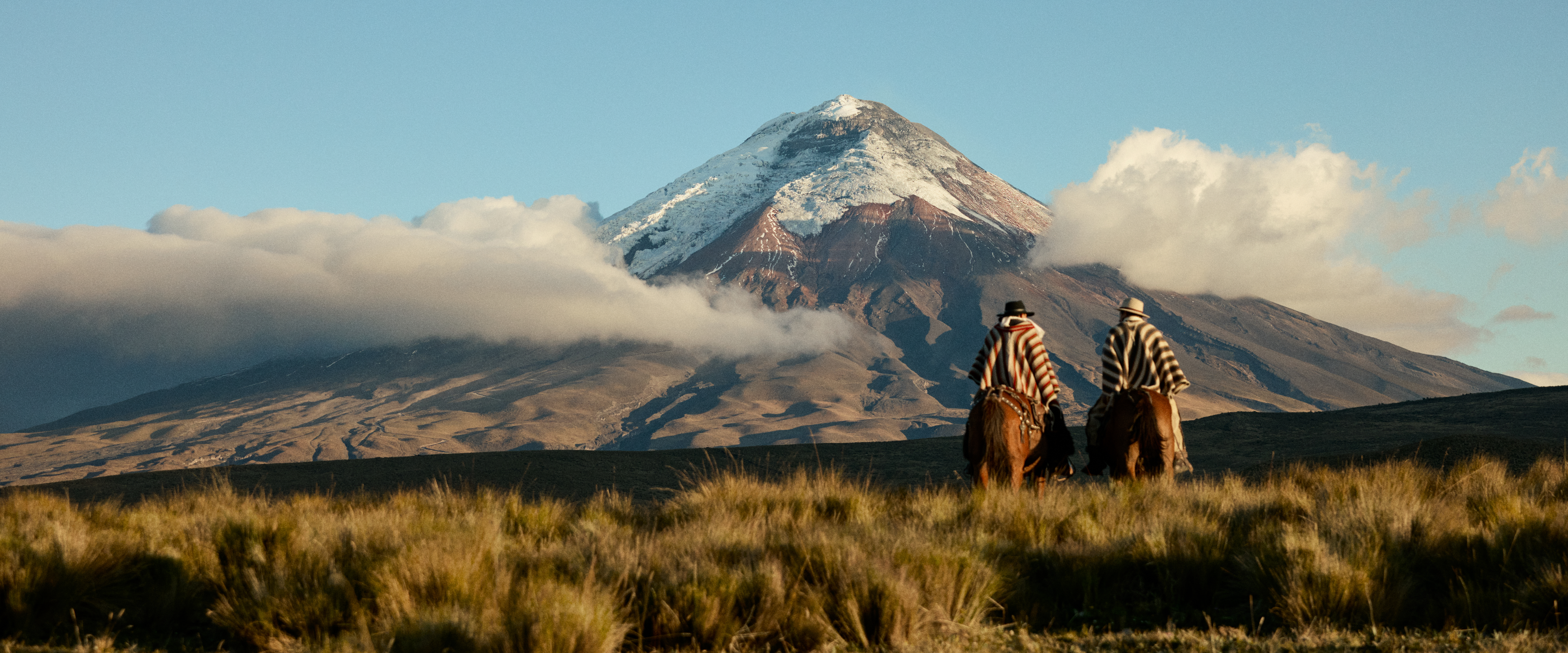 two people on horseback riding towards a mountain in Ecuador